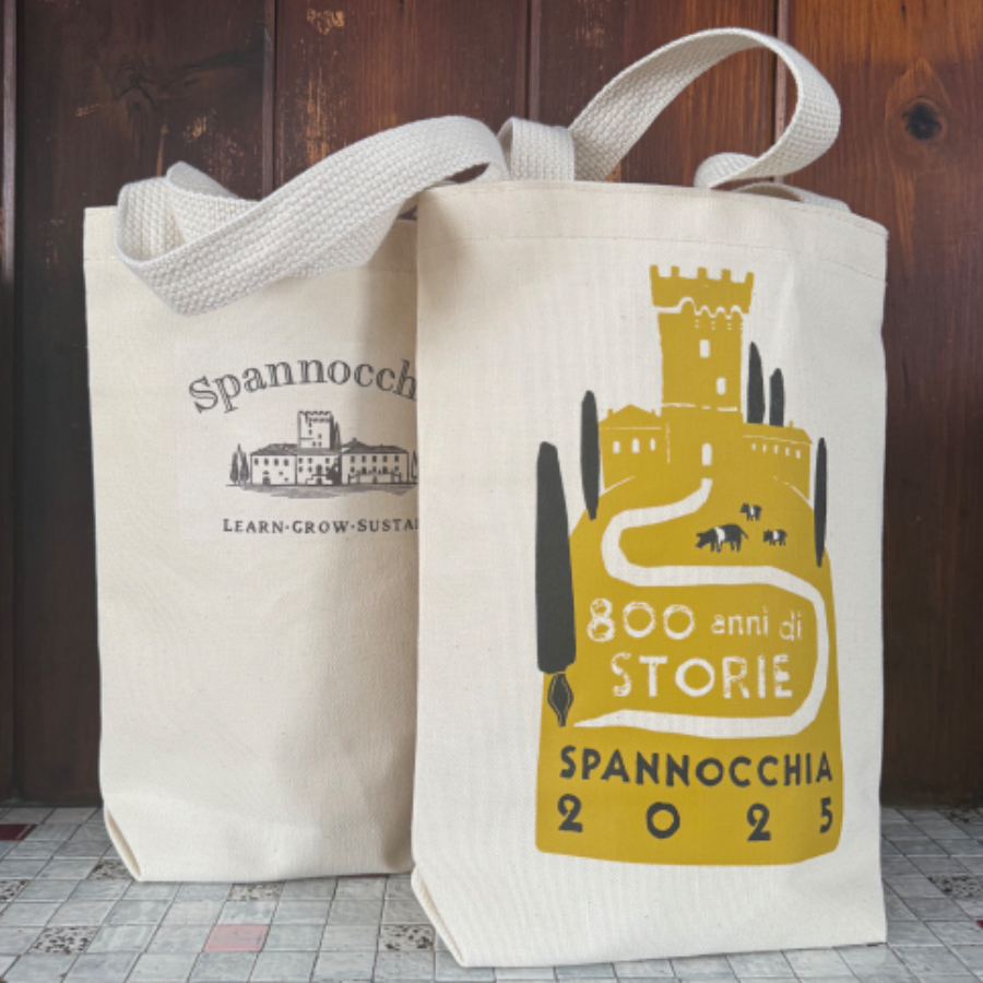 Two canvas tote bags with handles flopped over on a tiled surface. One bag shows the standard Spannocchia logo while the other showcases the special anniversary logo.