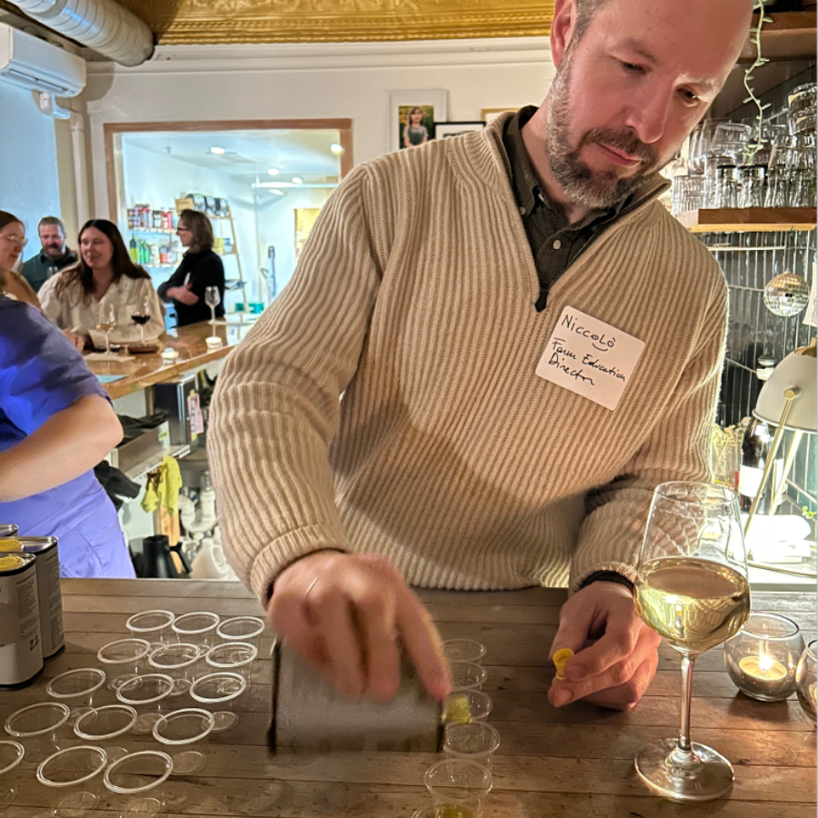 Niccolò standing behind a wood counter, pouring olive oil into small tasting cups. 